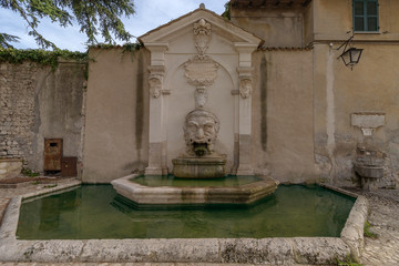 Old fountain (Fontana del Mascherone) on the wall of the thirteenth-century former church of Saints Simon and Jude in  Spoleto, Umbria, Italy