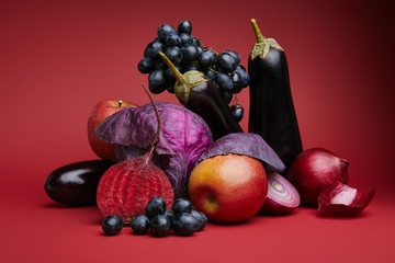 close-up view of fresh ripe grapes, apples, eggplants, beetroot, onions and cabbage on red