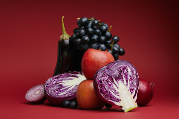 close-up view of apples, grapes, eggplant, cabbage and onions on red