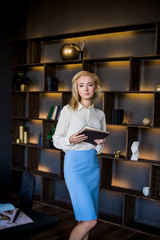 Beautiful young business woman stands near the table with documents. Business concept