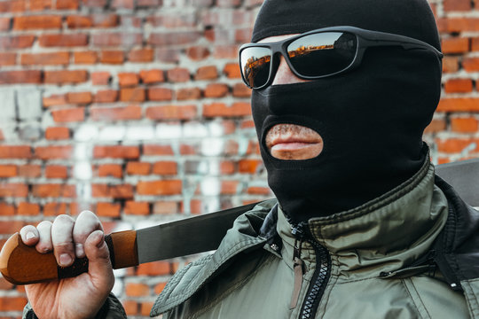 Commando in a mask and glasses with a machete in his hand against a brick wall