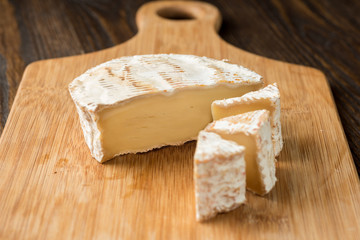 Brie cheese and tomato slice on wood cutting board.