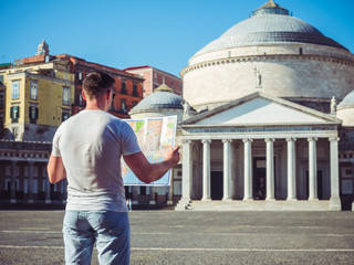 Handsome man holding a map against the background of the empty square in the beautiful city of Naples, Italy