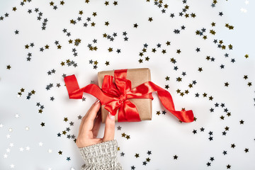 Female hands holding present with red bow on white background with delicate wavy ribbons and...