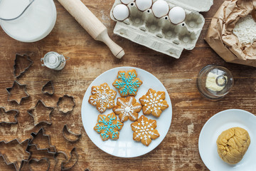 flat lay with Christmas cookies on plate, ingredients and cookie cutters arranged on wooden tabletop