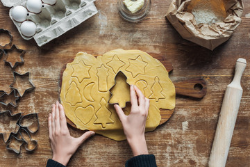 partial view of woman cutting raw dough with cookie cutter while preparing christmas cookies on...