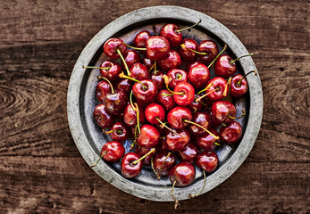 A metallic rustic bowl full of ripe Cherries over a wooden table.