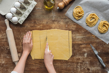 top view of female hands cutting dough for pasta on wooden table
