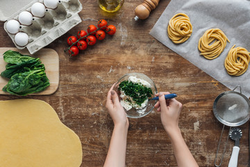 top view of female hands mixing spinach and creamy cheese in bowl on wooden table