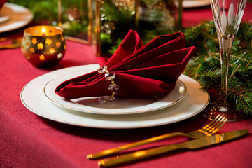 Beautiful served table with candles, Red tablecloth and napkins, white china, gold cutlery, crystal...