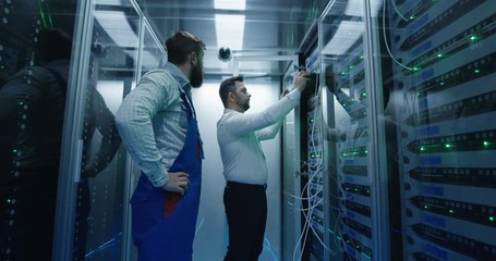 Medium shot of two men working in a data center taking networking equipment out for repair and maintenance