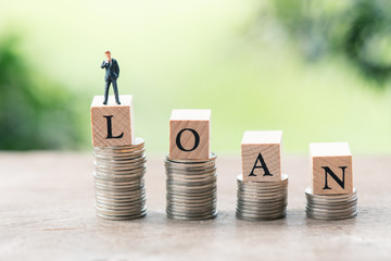 Miniature people businessmen standing with wood word LOAN stack of coins to thinking and planning....