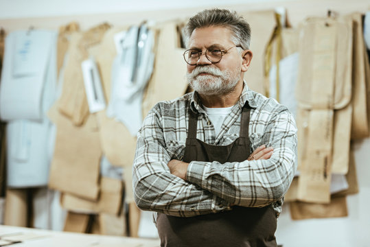 happy middle aged craftsman in apron and eyeglasses standing with crossed arms at studio - Powered by Adobe