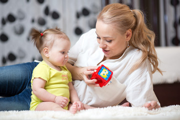 Babysitter and baby girl playing with toy cubes at home