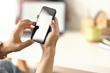 Closes-up male hand using mobile smart phone at desk workspace