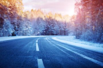 Fototapeta na wymiar winter road, covered with snow on sunny day. Black icy asphalt
