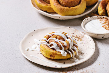Homemade pumpkin cinnamon bun rolls sweet autumn baked dessert with cream cheese sauce in spotted...