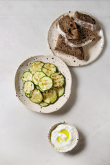 Grilled zucchini salad with yogurt dip and rye sliced bread in spotted ceramic plates over white marble background. Vegetarian food. Flat lay, space