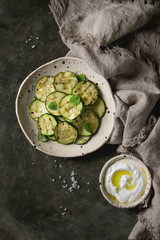 Grilled zucchini salad with yogurt dip in spotted ceramic plates on linen cloth textile over old dark metal texture background. Vegetarian food. Flat lay, space