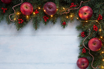 Christmas holiday background with red apples, red berries and bright garland on light blue wooden...