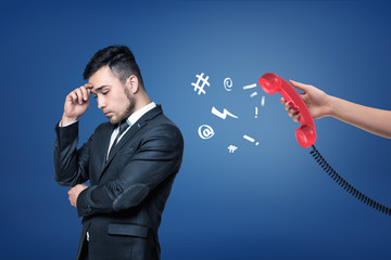 A tired businessman stands turned away from a red retro phone in a female hand.