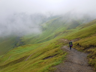 Hiking in cloudy Alps mountains. Woman Traveler with Backpack hiking in the Mountains. mountaineering sport lifestyle concept