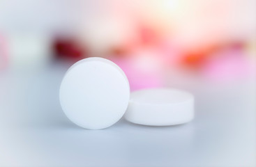 close up white pills with white ground and blurred colorful pills background