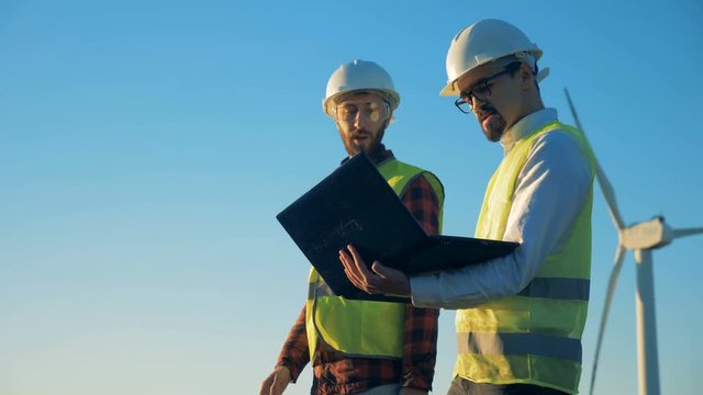 Male workers are walking in sunlight along the windmill.