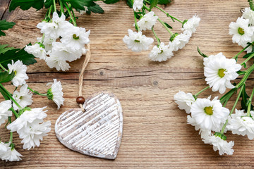 Wooden heart among daisy flowers.
