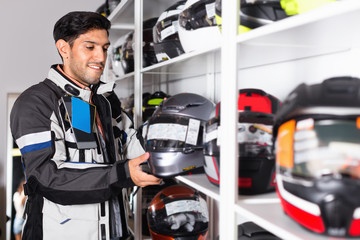 Male customer is choosing modern helmet near shelves