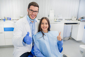 Dentist doctor and little girl smiling at camera. Thumb up