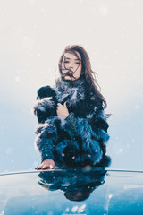 Winter portrait of young beautiful brunette woman wearing fur coat  in cabrio. Snowing winter...
