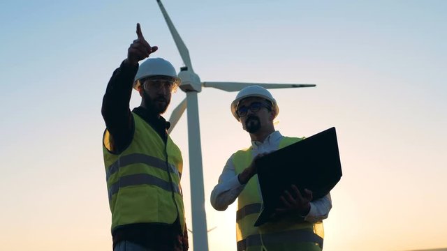 Two male experts are having a discussion in front of windmill. Clean, eco-friendly energy concept.