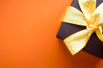 Brown gift box with yellow ribbon on orange background. Top view with copy space.