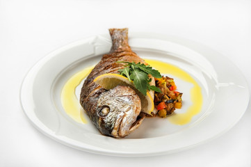 Grilled dorade on a white plate with sauce, arugula on a white plate isolated on white background
