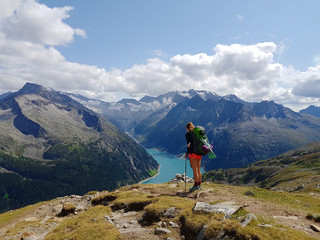 Hiker with backpack relaxing on top of a mountain and enjoying valley view with lake during trip in the alps
