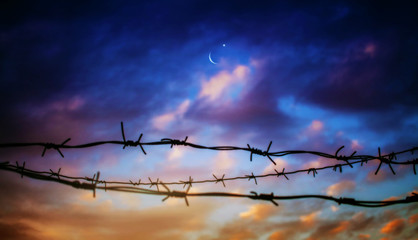 the ban in Islam .  behind barbed wire . Crescent Moon on a night sky . Sunset and new moon . 