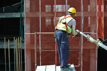 Construction workers wearing safety harness and installing scaffolding at high level in the construction site. 