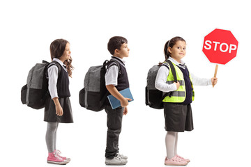 Schoolchildren waiting in line with one of them wearing a safety vest and holding a stop sign