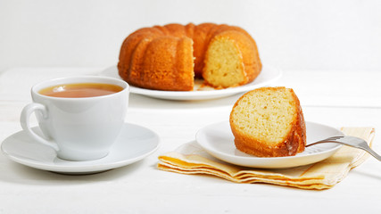 Closeup homemade lemon cake soaked with lemon syrup and cup of tea on white wooden table. Shallow focus.