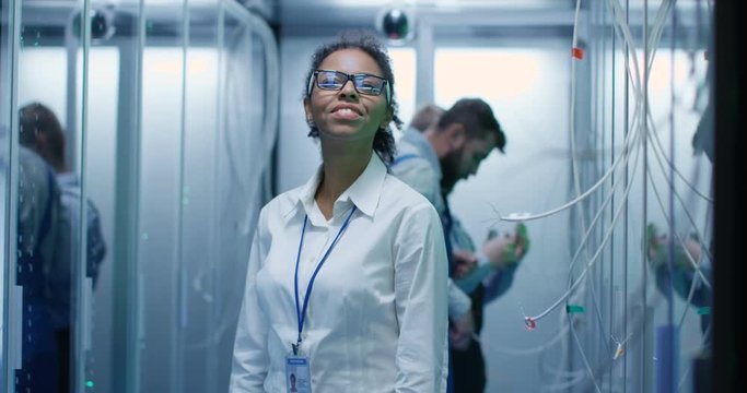 Medium shot of a female manager smiling at the camera while working in a data center inbetween rows of server racks