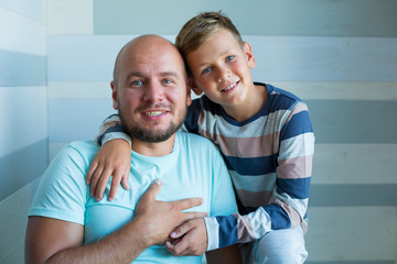 Side view of handsome father and his cute son looking at each other and smiling while spending time together at home. Blue eyes and plenty blue color tones.