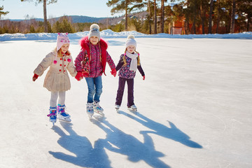Three little girl friends learn to skate.  Outdoor recreation and holidays