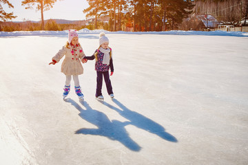 Two little girls hold hands and skate.Space for text