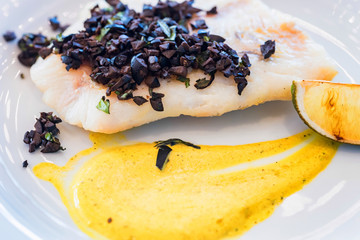 Pike perch fillet with vegetables and olives on white plate