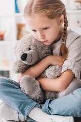 close-up portrait of depressed little child embracing her teddy bear