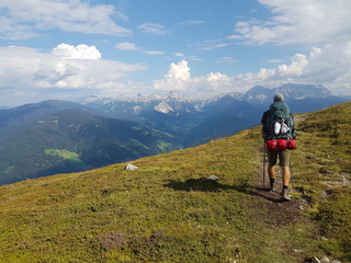 Hiker with backpack walking a grass trail on top of a mountain and enjoying valley view during trip in the alps