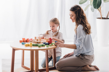 side view of happy mother playing blocks with adorable little child
