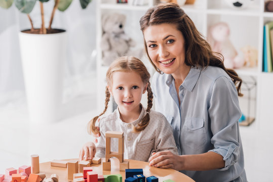 smiling mother and child looking at camera while playing with blocks