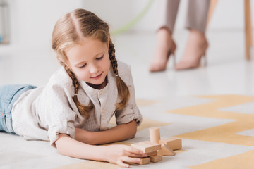 little child playing with wooden blocks on floor with blurred psychologist sitting on background